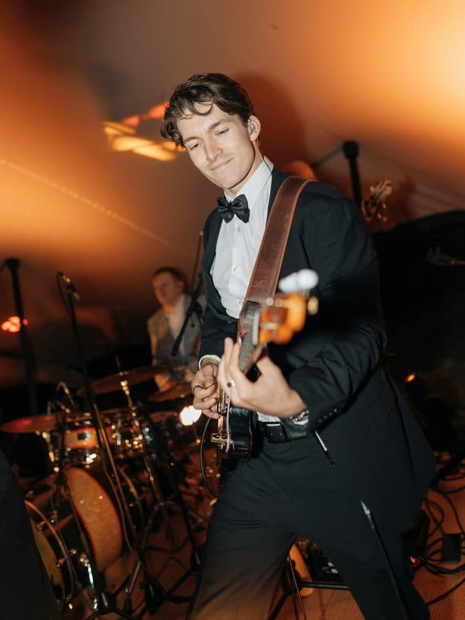 The uploaded photograph: a guitarist in a dinner jacket and bow tie playing on a dim stage, a drummer behind him